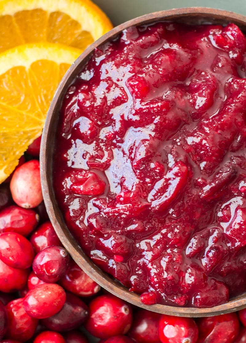 overhead view of keto cranberry sauce in a wood bowl next to orange slices and fresh cranberries 