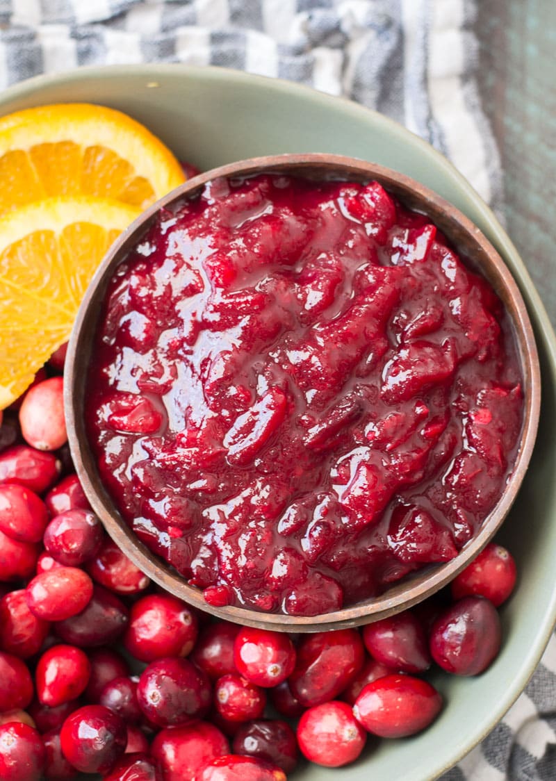 overhead view of low carb cranberry sauce in a wood bowl on a plate with orange slices and fresh cranberries 