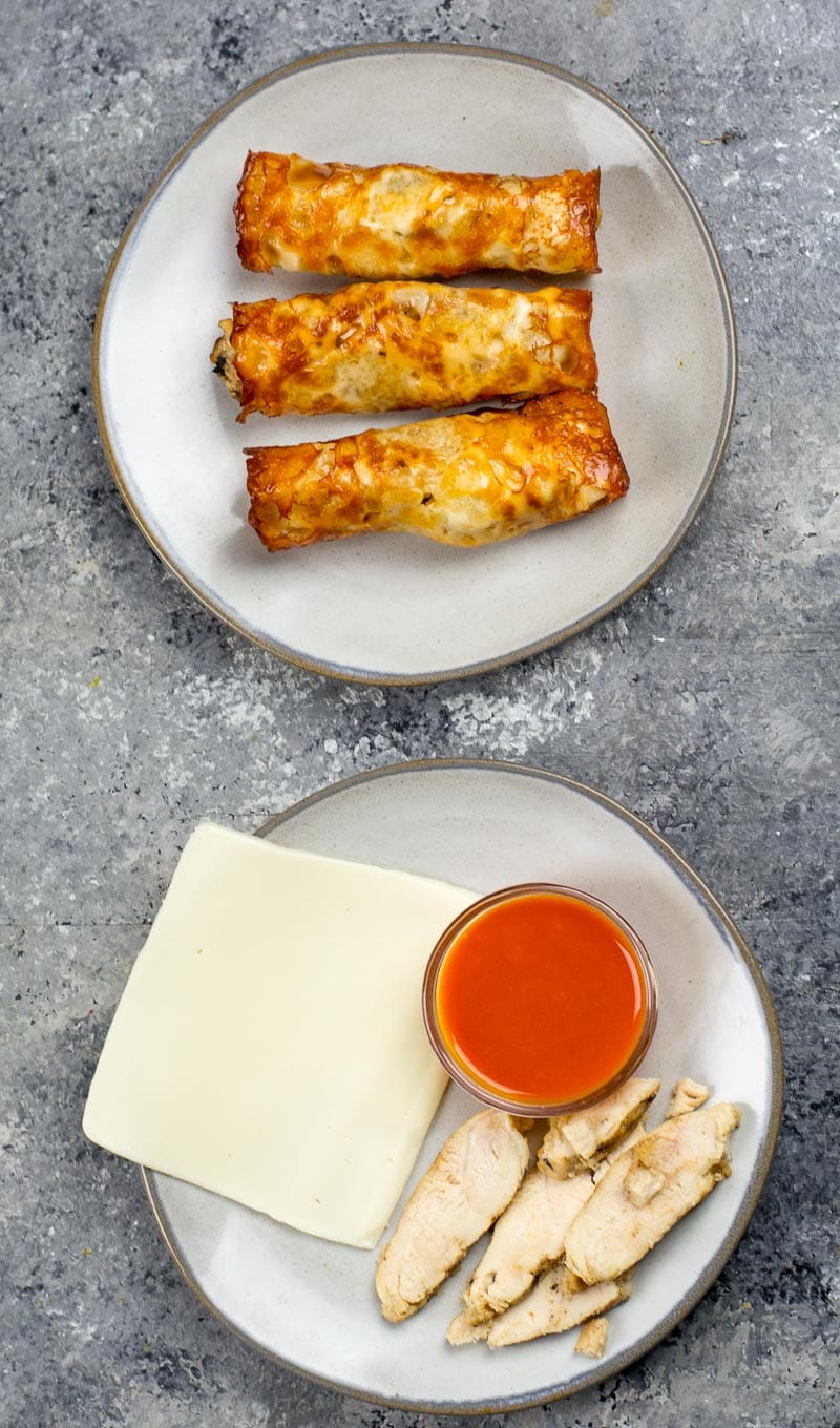 Overhead view of three keto buffalo chicken taquitos on a white plate. Another plate has the raw ingredients. 