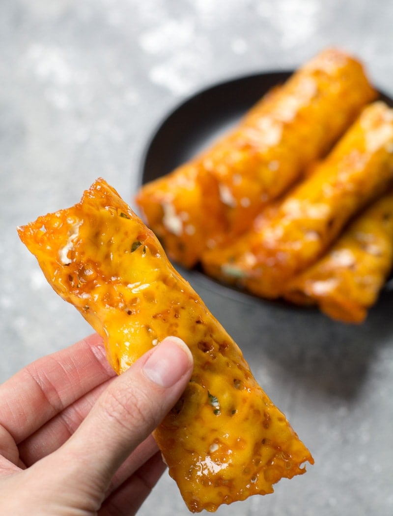 a keto jalapeño popper being held aloft over a plate of homemade taquitos 