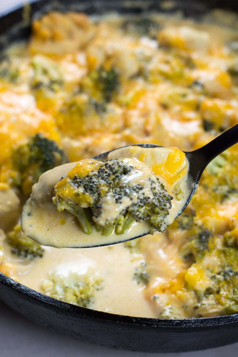 A spoonful of low carb chicken broccoli casserole being held over a skillet. 