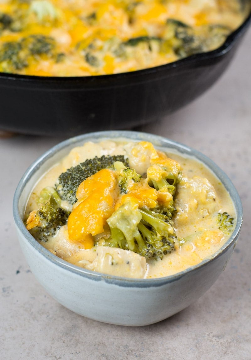 A serving of low carb cheesy chicken and broccoli in a bowl. A skillet is in the background. 