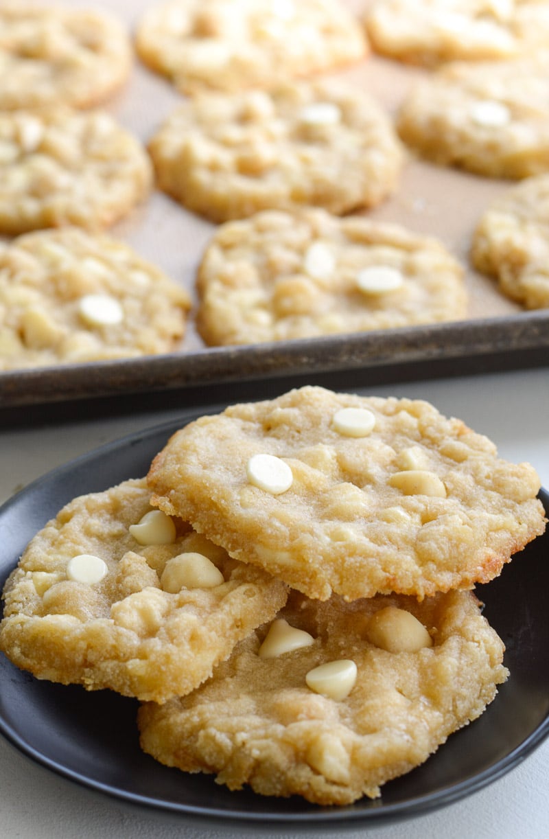 three keto macadamia nut cookies on a small plate. extra cookies are on a baking sheet in the background. 