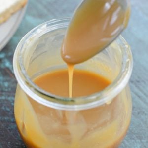 A jar of keto caramel sauce with a spoon hovering over it.