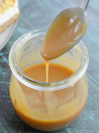 A jar of keto caramel sauce with a spoon hovering over it.