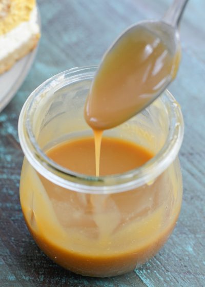 A jar of keto caramel sauce with a spoon hovering over it.