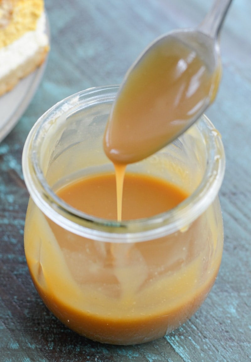 A jar of keto caramel sauce with a spoon hovering over it.