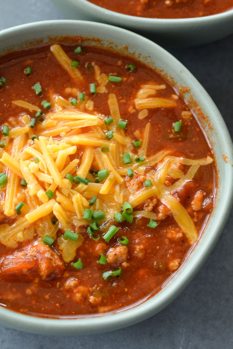 Overhead view of no bean chili in a bowl, topped with chives and shredded cheddar cheese. 