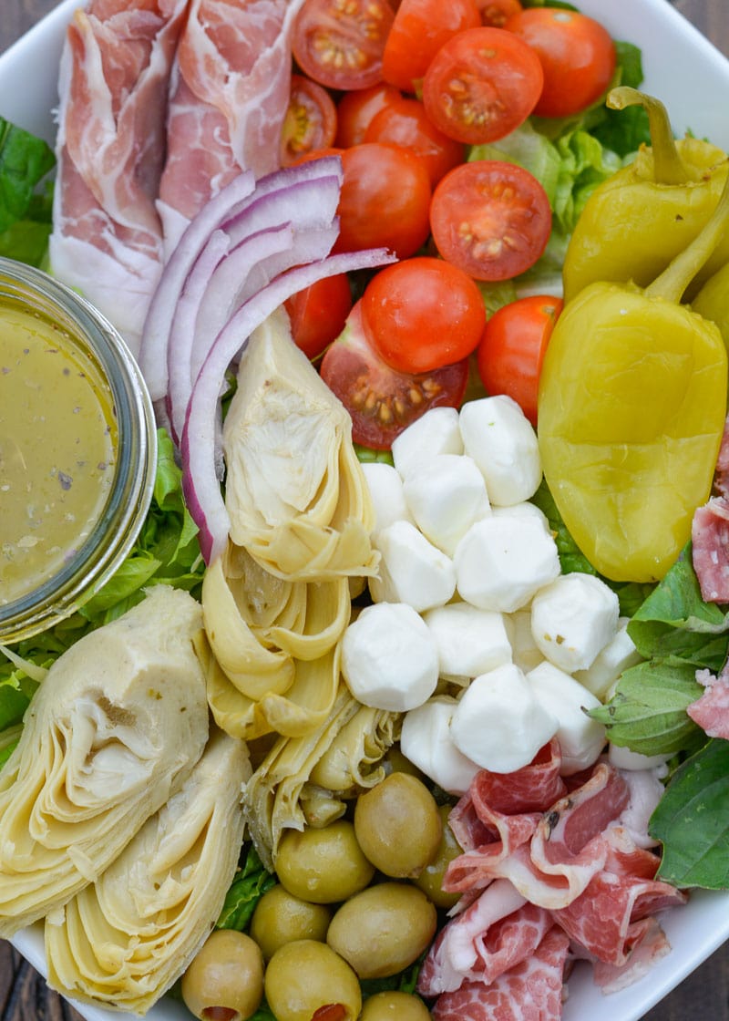 antipasto salad in a white dish with dressing on the side