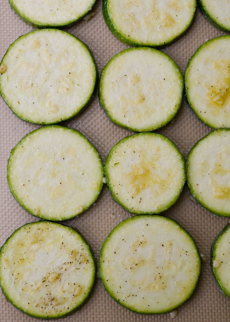 Overhead view of seasoned zucchini slices arranged on silpat