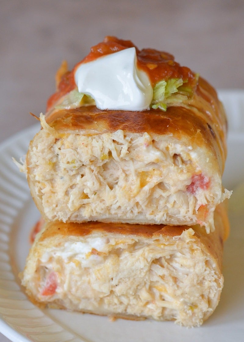 Two halves of a chimichanga stacked on a plate, topped with sour cream and salsa