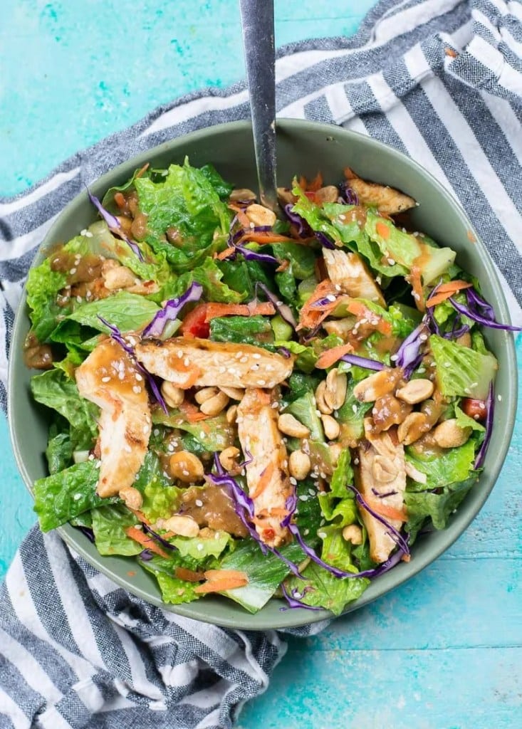 thai salad topped with chicken and peanut dressing in a green bowl on a blue background