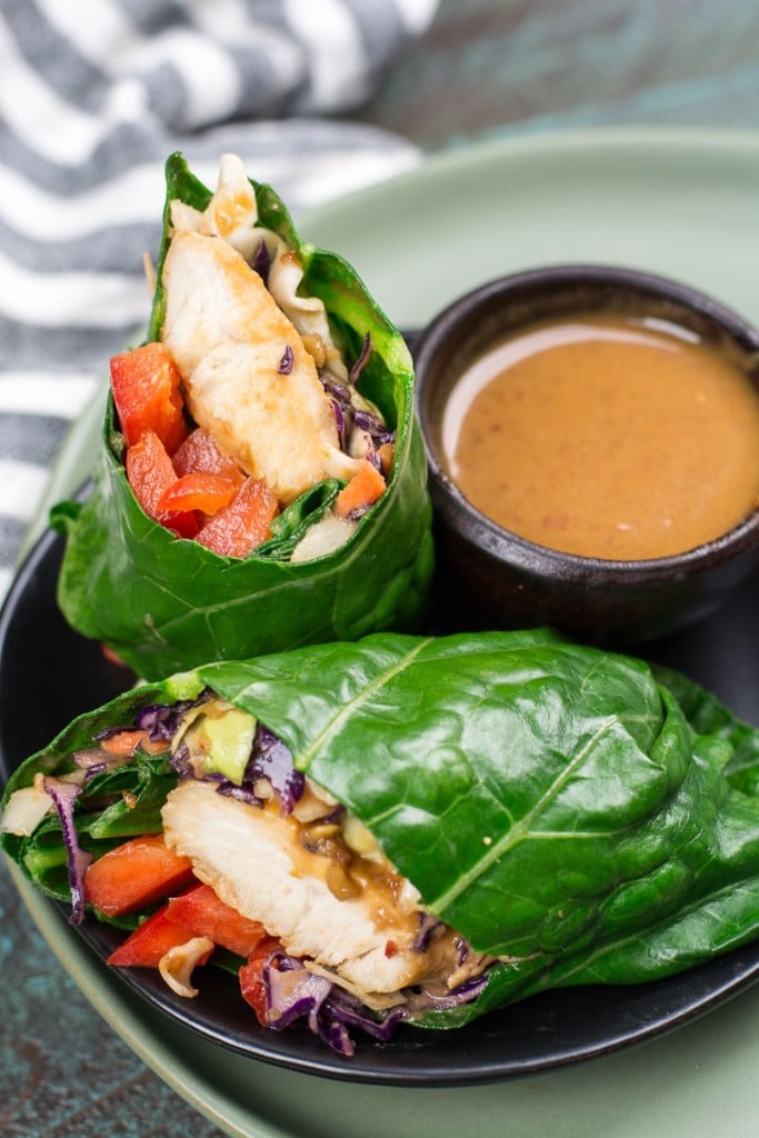 thai chicken collard wrap, sliced in half and presented on a black plate with peanut sauce in a bowl on the side