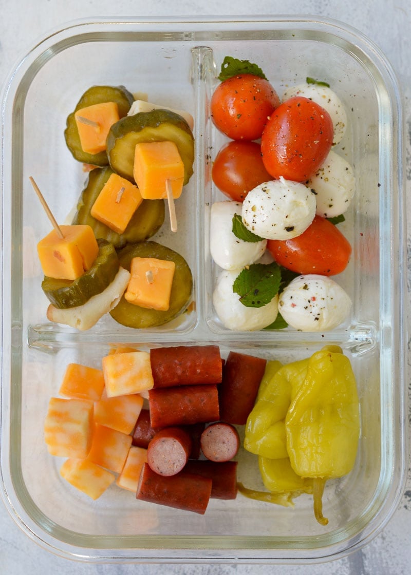 lunch skewers in a glass lunch container with caprese salad, pepperoncini, sausages, and cheese
