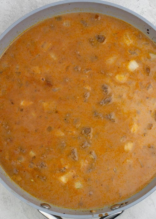 broth, milk, and spices added to a pan with beef, onions, and tomato sauce for hamburger helper.