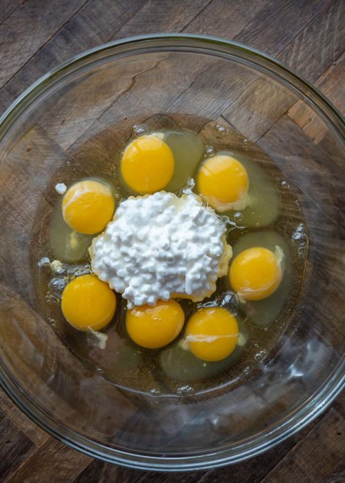 A mixing bowl with seven eggs and some cottage cheese in it