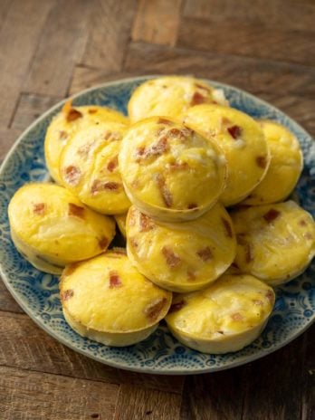 A plate full of egg bites with pieces of bacon