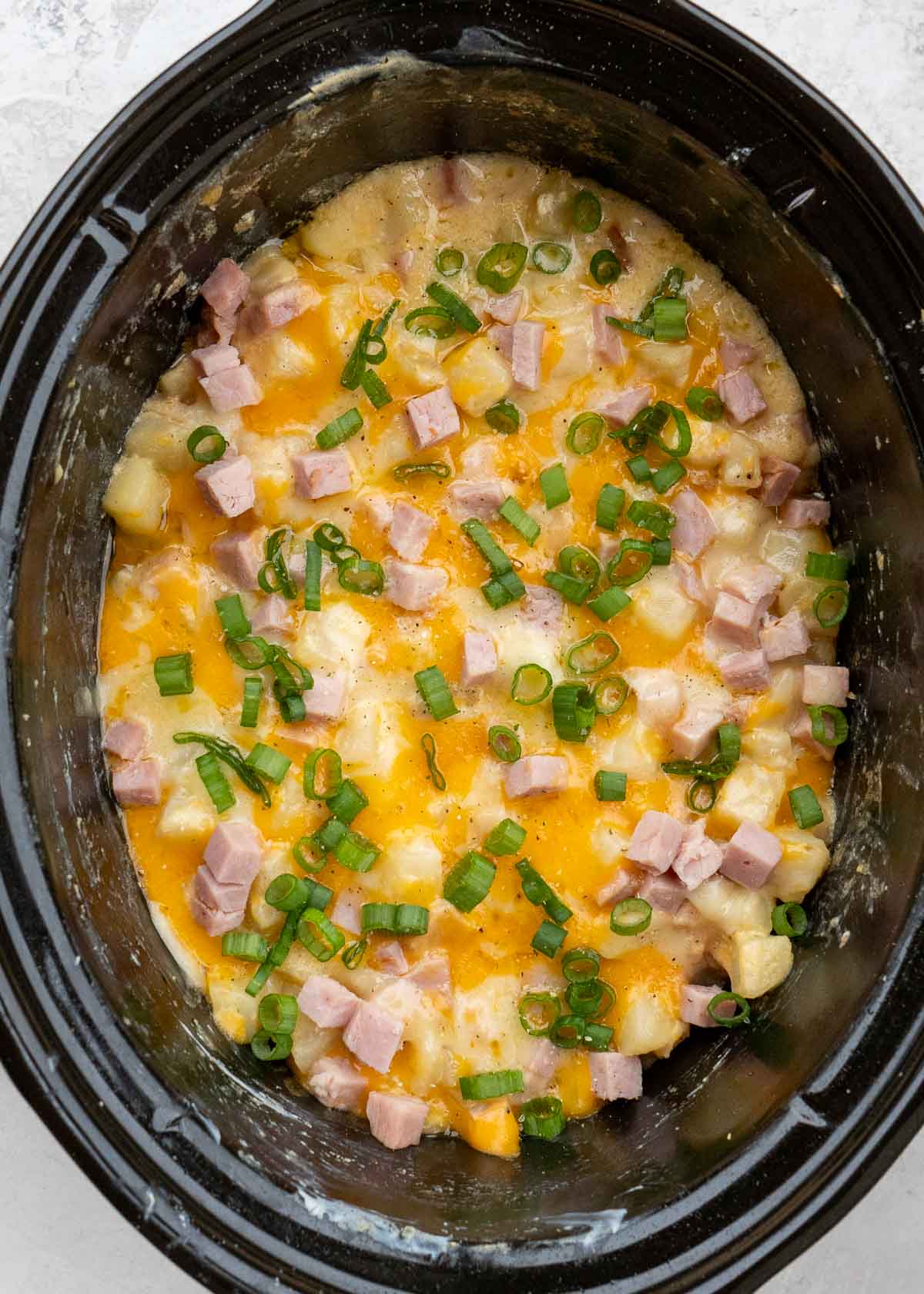 Cheesy Hashbrown Casserole is the perfect comfort food! Frozen hashbrowns are paired with sour cream, cheddar cheese, and ham to make the ultimate side dish! This simple potato recipe requires no prep work and can be made in the crock pot or oven!