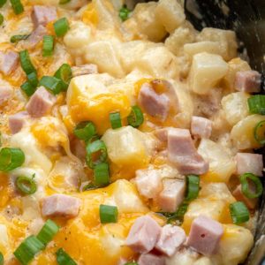 Cheesy Hashbrown Casserole is the perfect comfort food! Frozen hashbrowns are paired with sour cream, cheddar cheese, and ham to make the ultimate side dish! This simple potato recipe requires no prep work and can be made in the crock pot or oven!