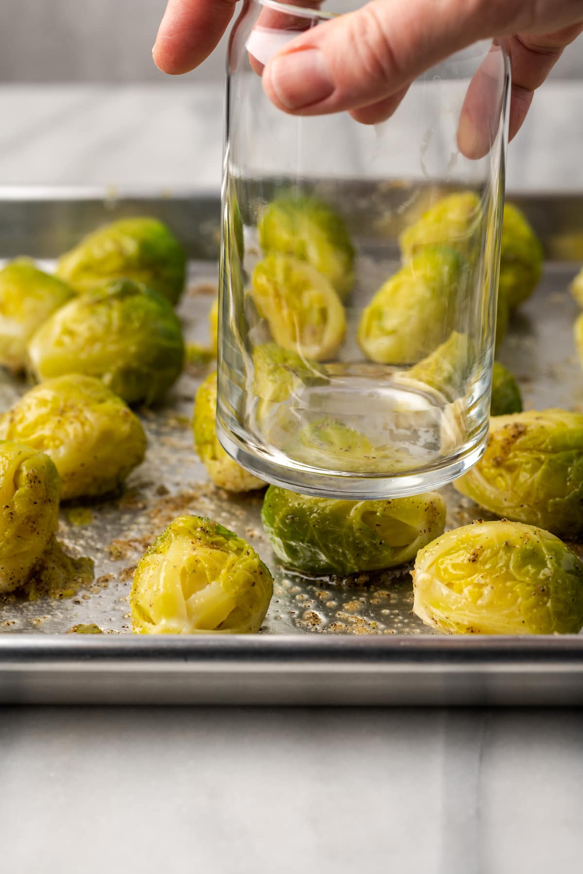 Using the bottom of a glass to smash a Brussels sprout on a sheet pan