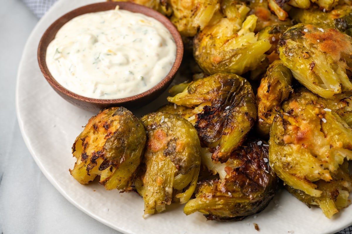 Closeup of crispy smashed Brussels sprouts on plate with small bowl of lemon aioli