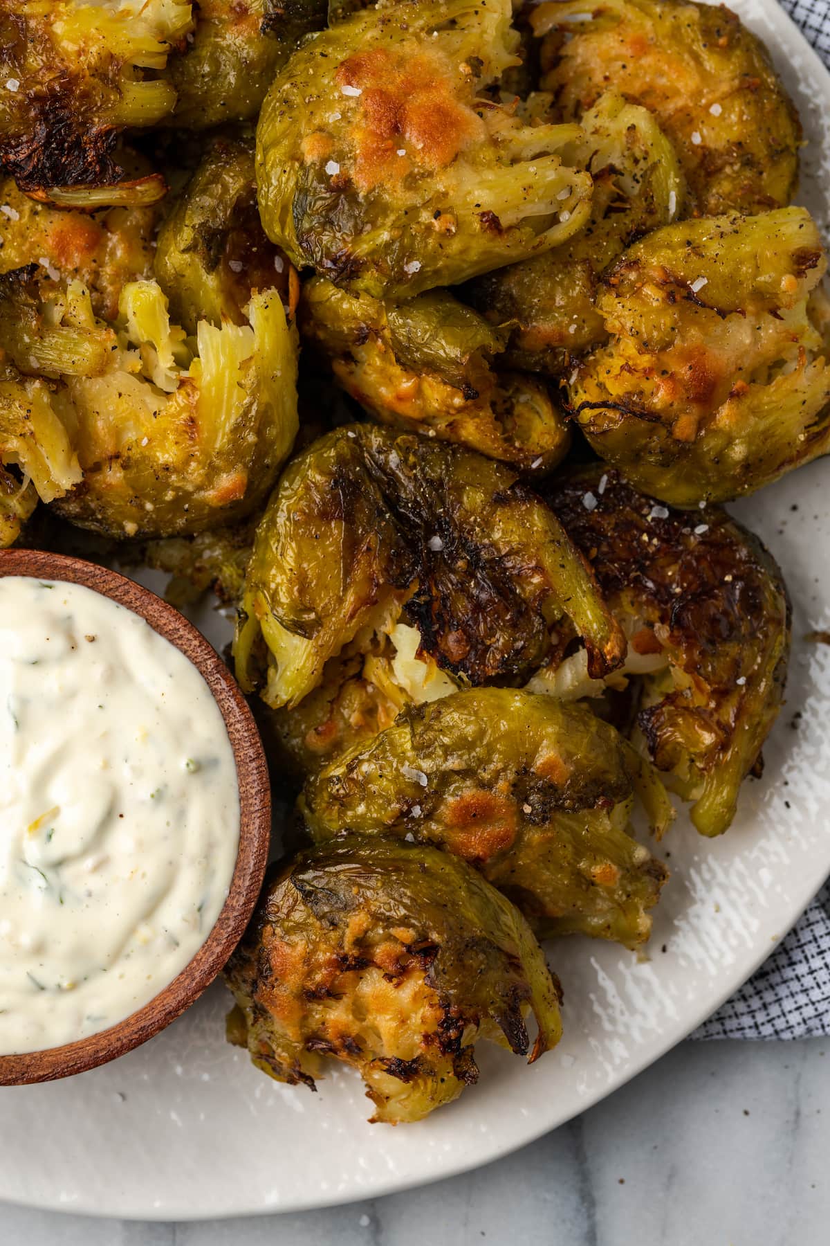 Overhead view of smashed Brussels sprouts on plate with bowl of lemon aioli