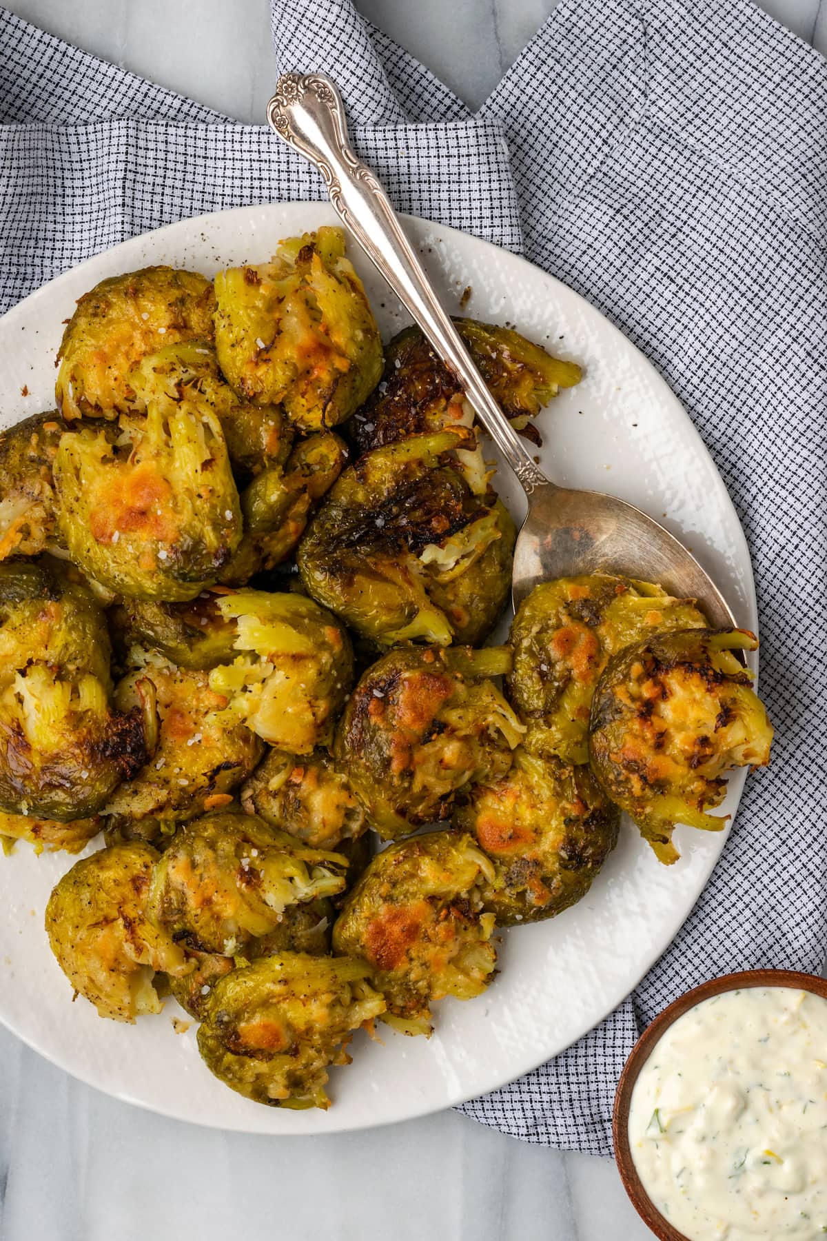 Overhead view of smashed Brussels sprouts on plate with spoon, with small bowl of lemon aioli on the side