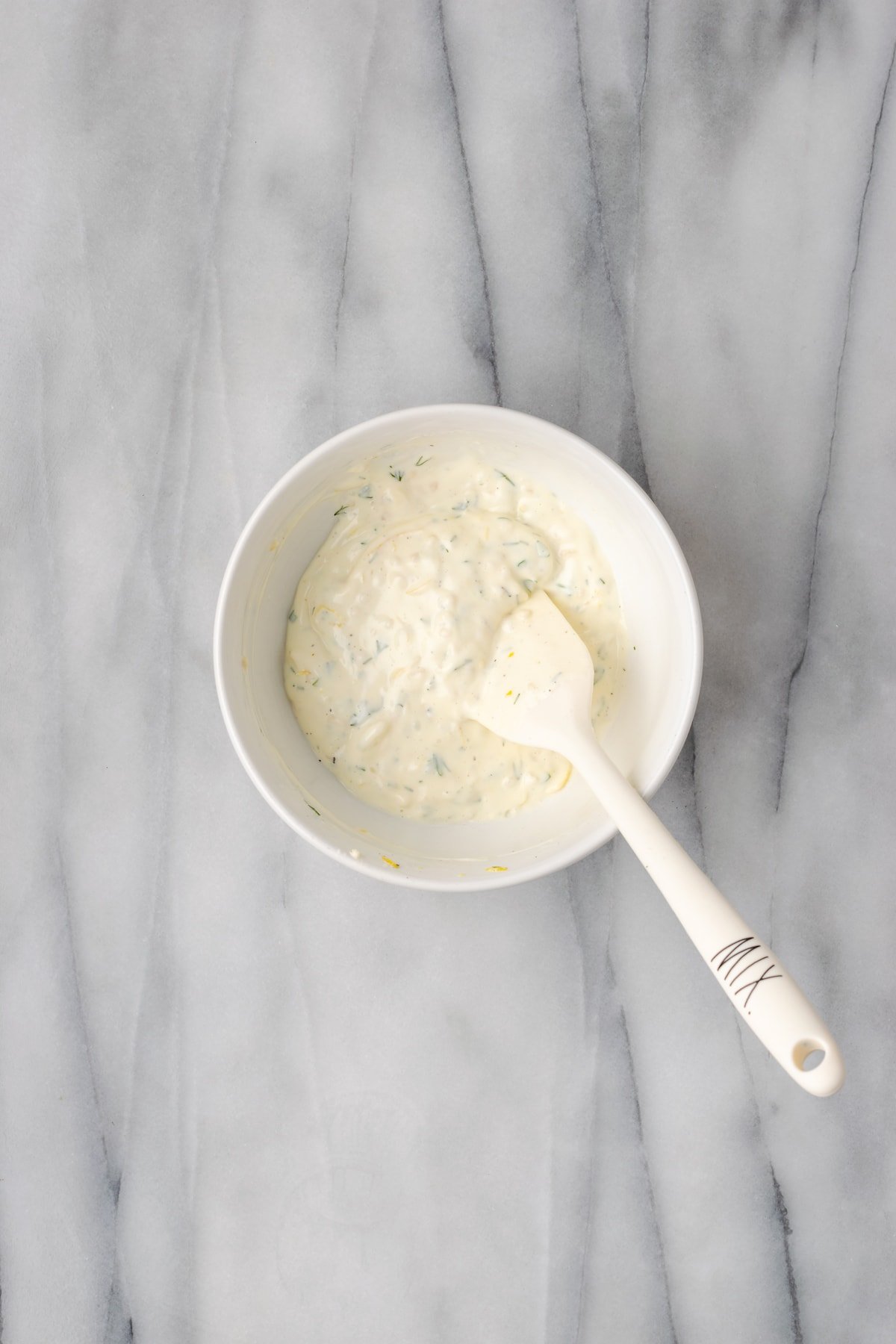 Overhead view of mixing spoon in bowl of lemon aioli