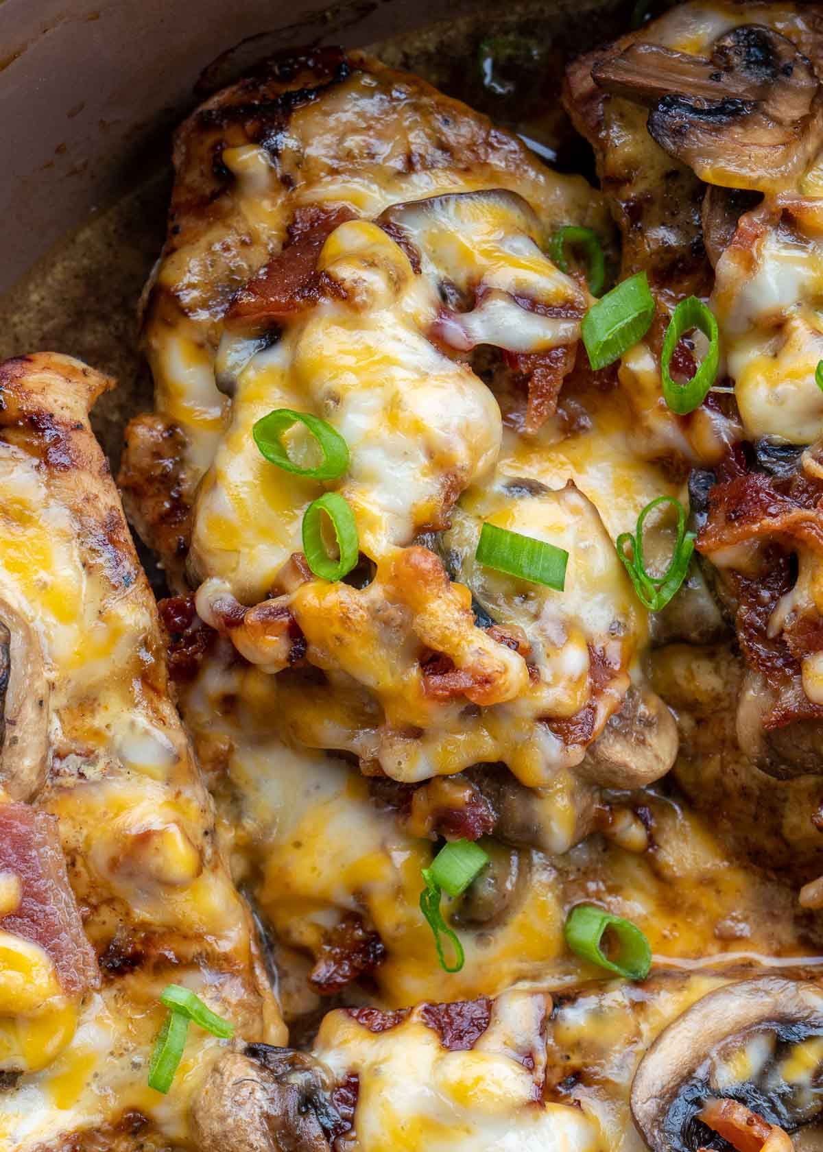 Green onions being added to cheese and bacon covered chicken