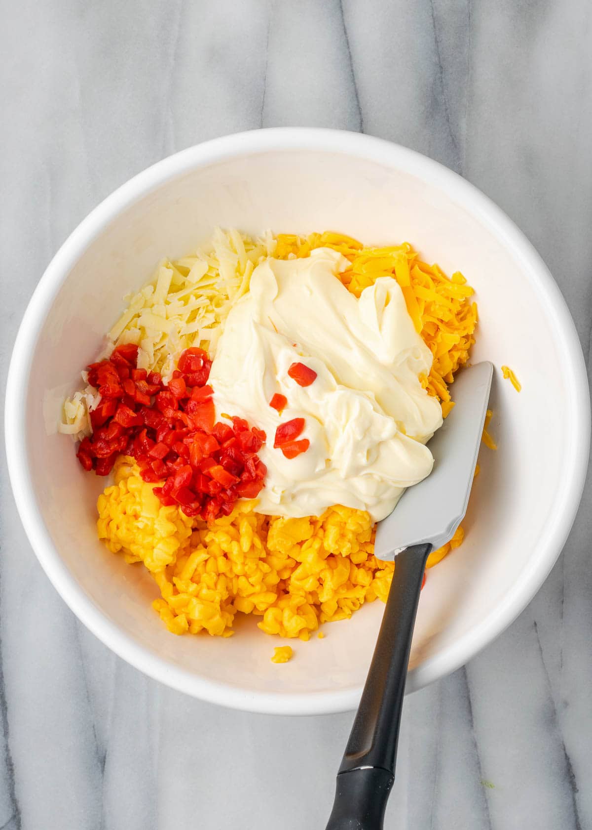 Pimento cheese ingredients being mixed in white mixing bowl