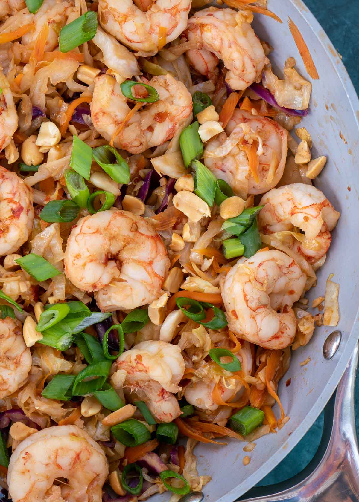 Close up of the edge of a pan full of shrimp stir fry topped with scallions