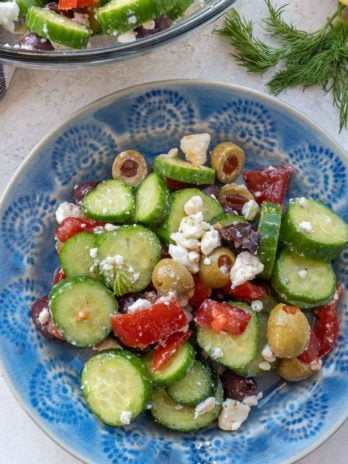 Overhead view of cucumber salad on blue patterned plate with bowl of salad in background