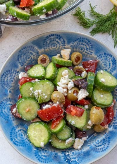 Overhead view of cucumber salad on blue patterned plate with bowl of salad in background