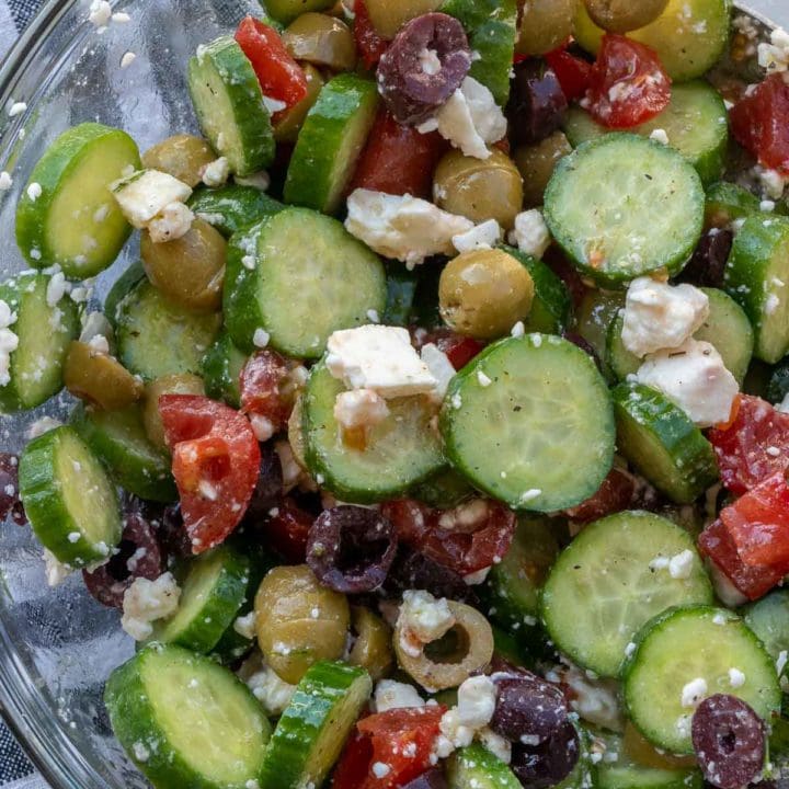 Overhead view of cucumber salad with olives, tomatoes, and feta in glass bowl
