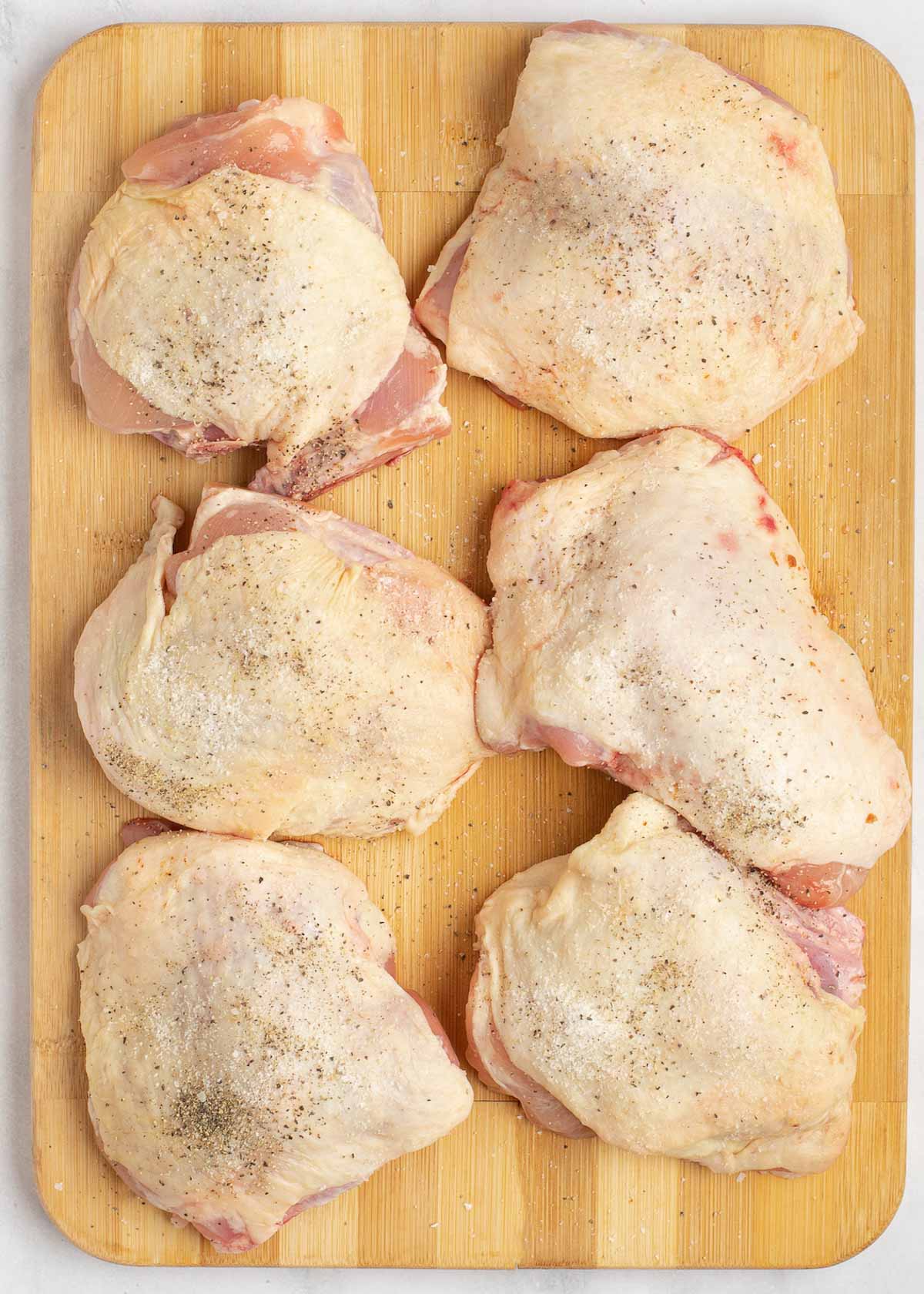 bone-in, skin-on chicken thighs seasoned with salt and pepper on a cutting board