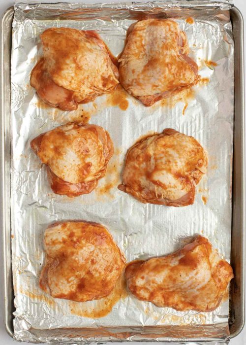 marinated and seasoned chicken thighs on an aluminum foil-lined baking pan