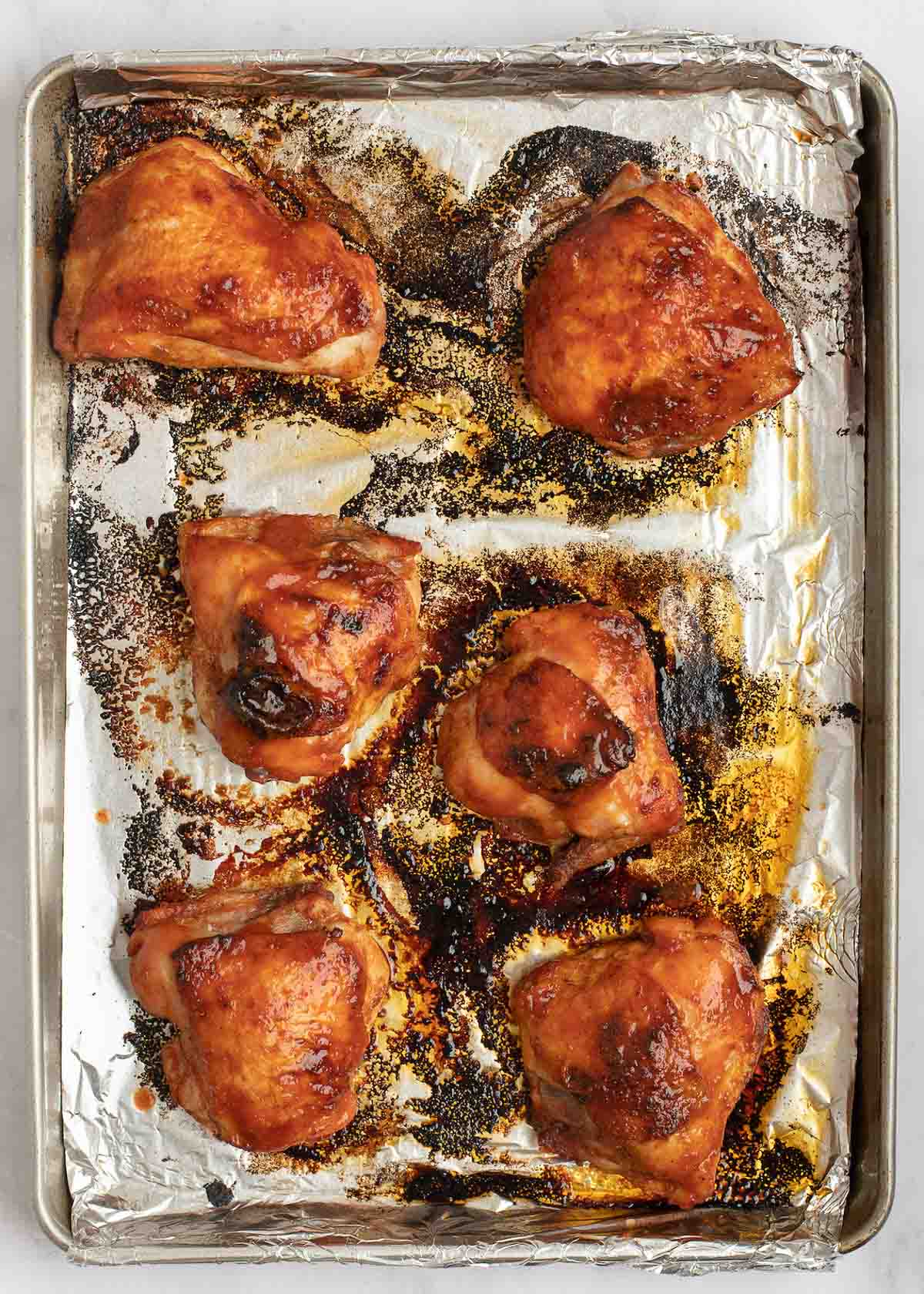 baked chicken thighs with homemade bbq sauce on an aluminum foil lined baking sheet