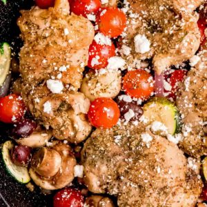 mediterranean chicken and veggies in a cast iron skillet, sprinkled with feta cheese