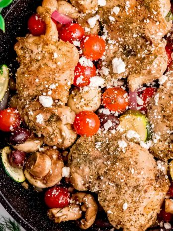 mediterranean chicken and veggies in a cast iron skillet, sprinkled with feta cheese