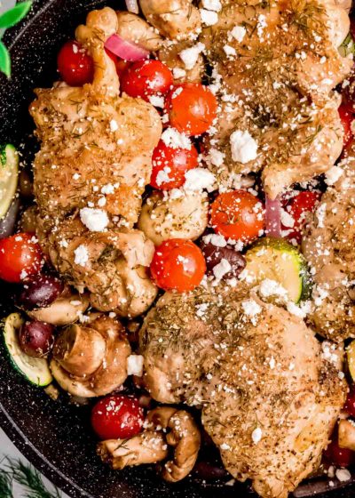 mediterranean chicken and veggies in a cast iron skillet, sprinkled with feta cheese