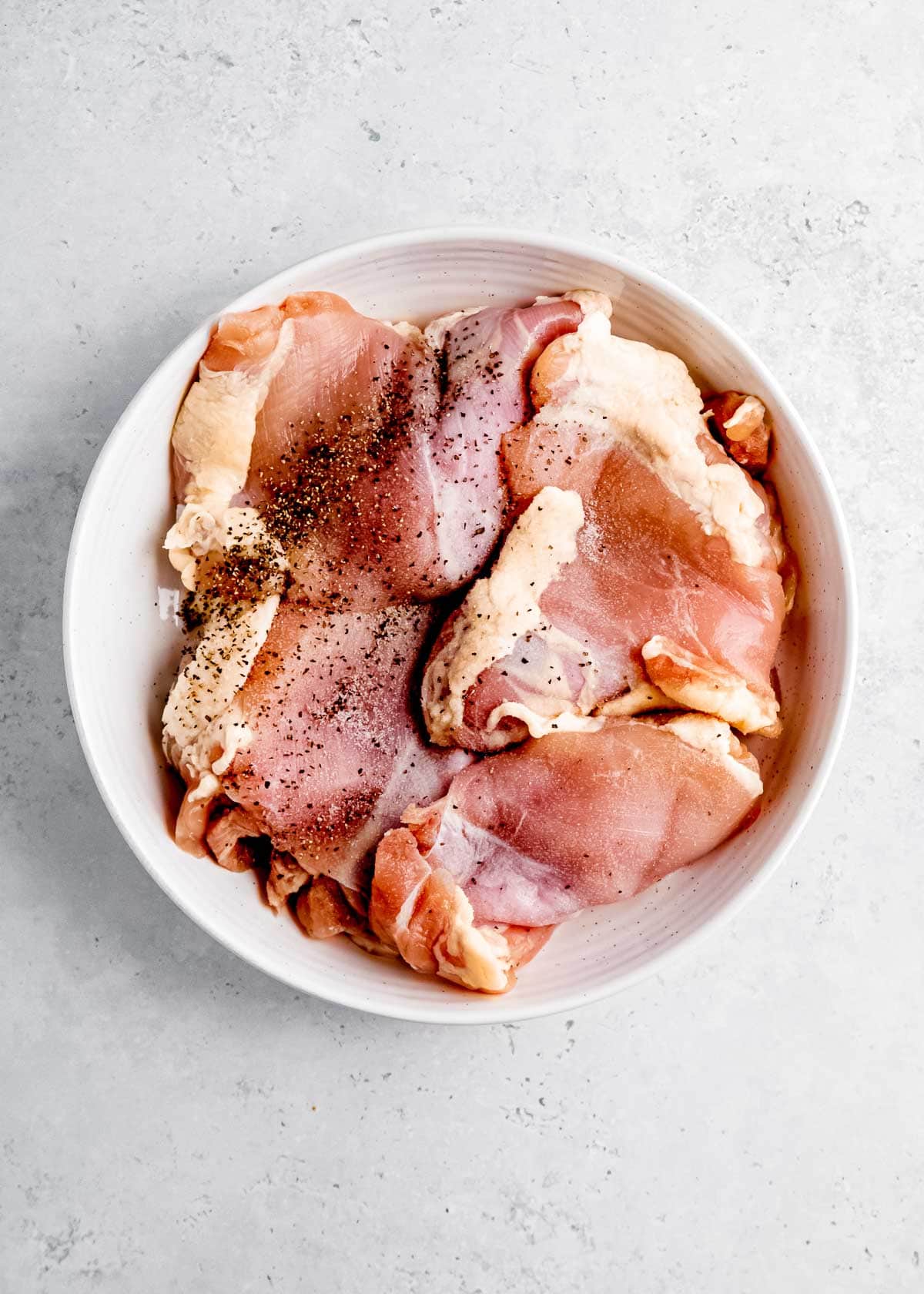 chicken thighs seasoned with salt and pepper in white bowl