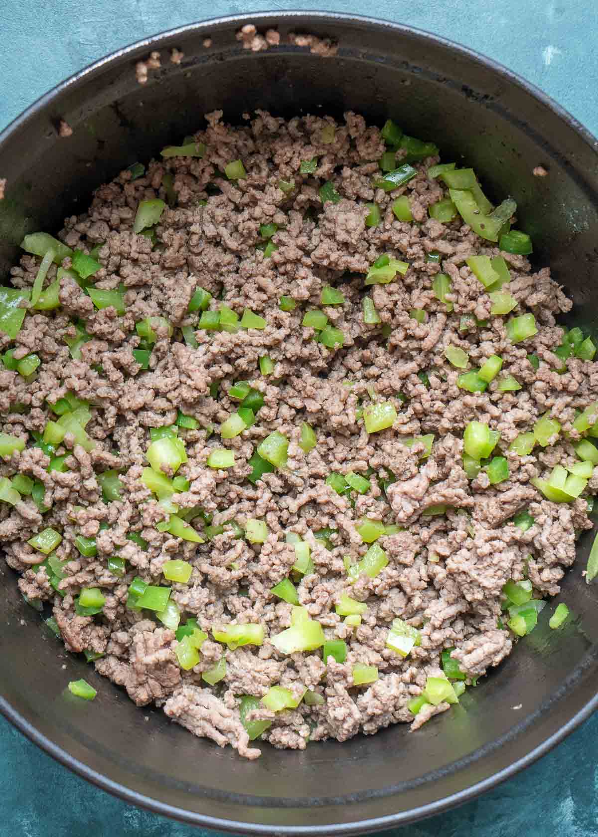 browned ground beef with chopped bell peppers and jalapenos in a cast iron dutch oven