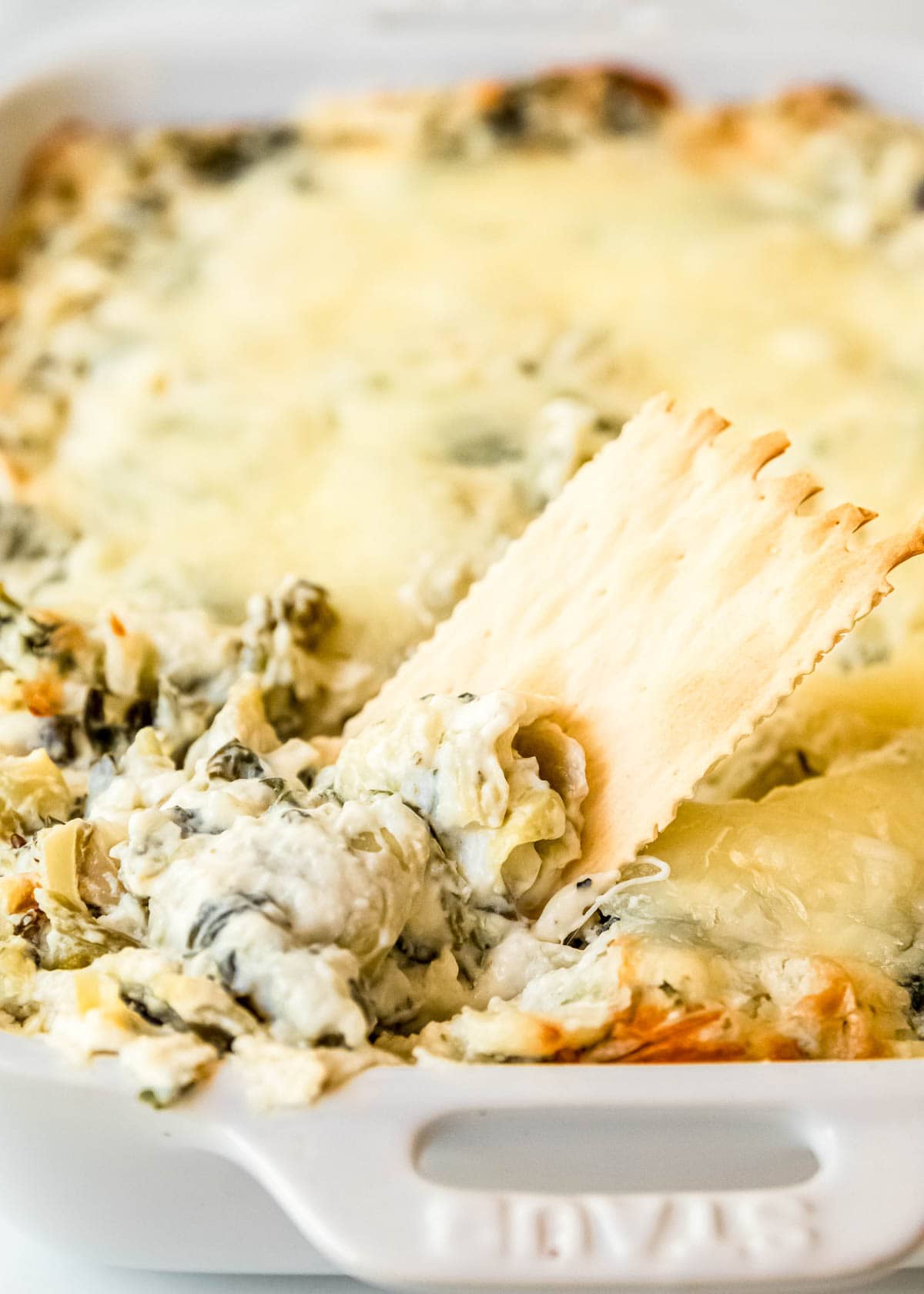 spinach artichoke dip being scooped up onto a cracker