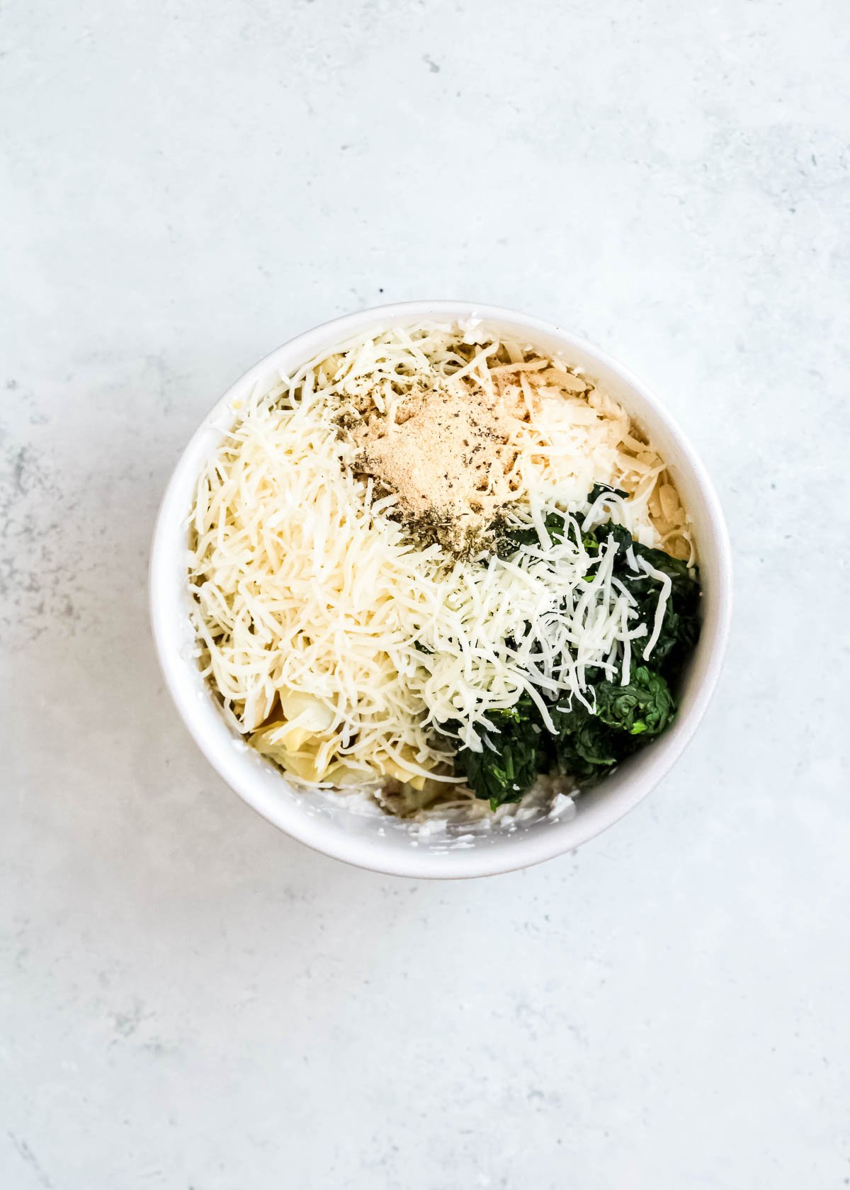 spinach, cheese, seasonings, chopped artichokes in a bowl with cream cheese, mayonnaise, and yogurt in a white bowl