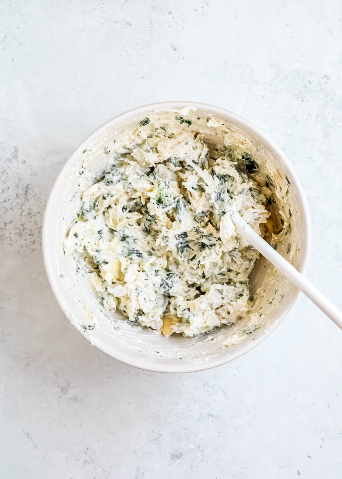 mixed up cream cheese, mayonnaise, yogurt, spinach, artichokes, seasonings, and cheese in a white bowl