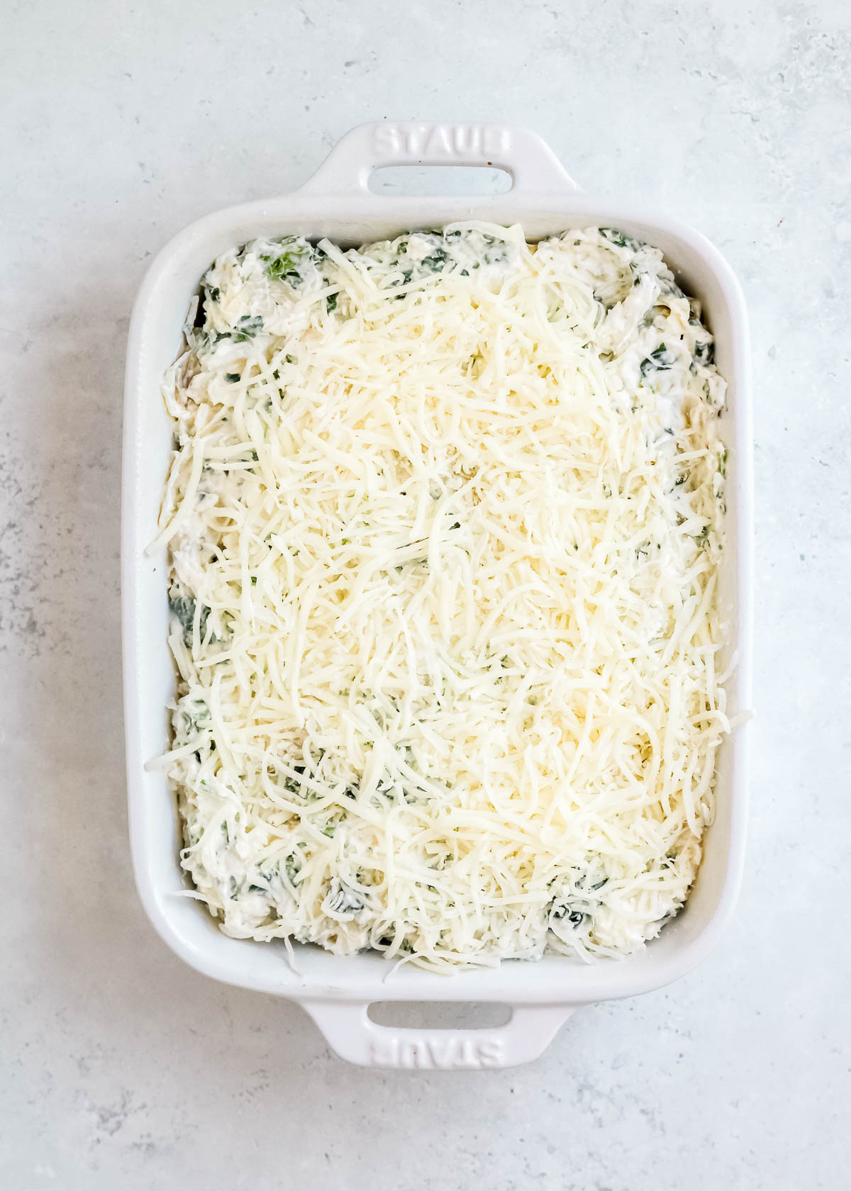 spinach dip topped with shredded cheese in a white rectangular baking dish