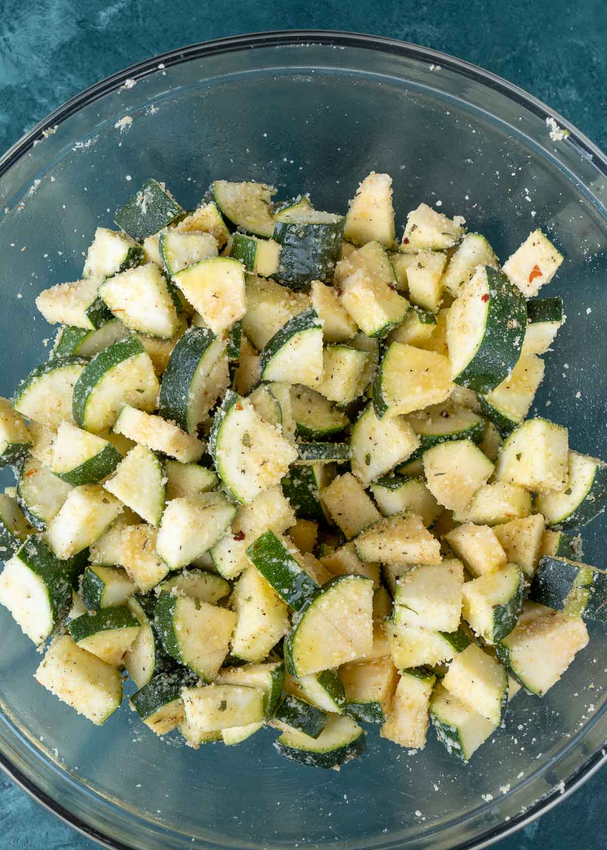 zucchini quarters mixed with oil, seasonings, and parmesan in a glass bowl