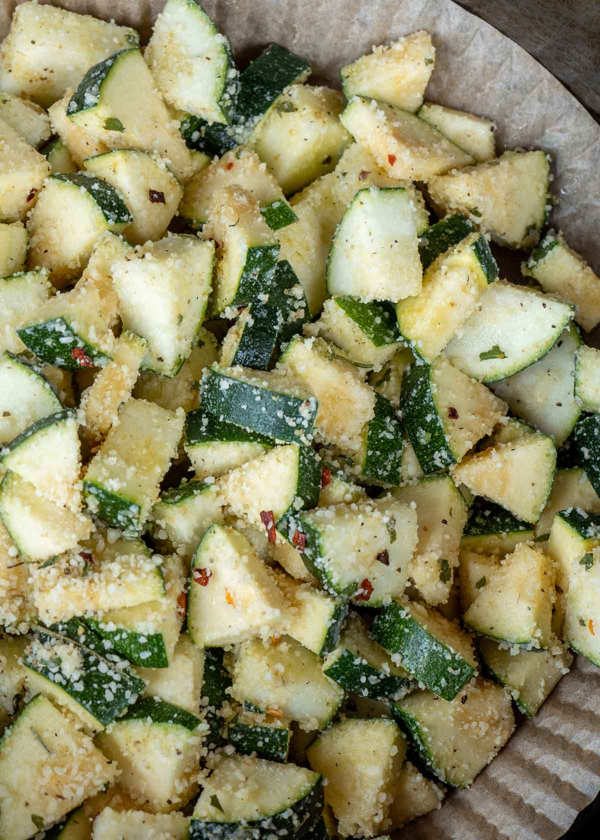 zucchini covered in seasonings and parmesan in an air fryer with a liner