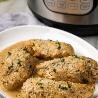 tender instant pot chicken breast with a pan sauce on a plate with instant pot in background
