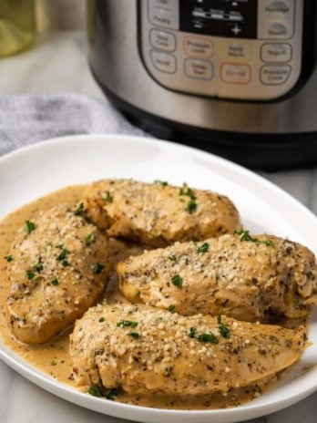 tender instant pot chicken breast with a pan sauce on a plate with instant pot in background